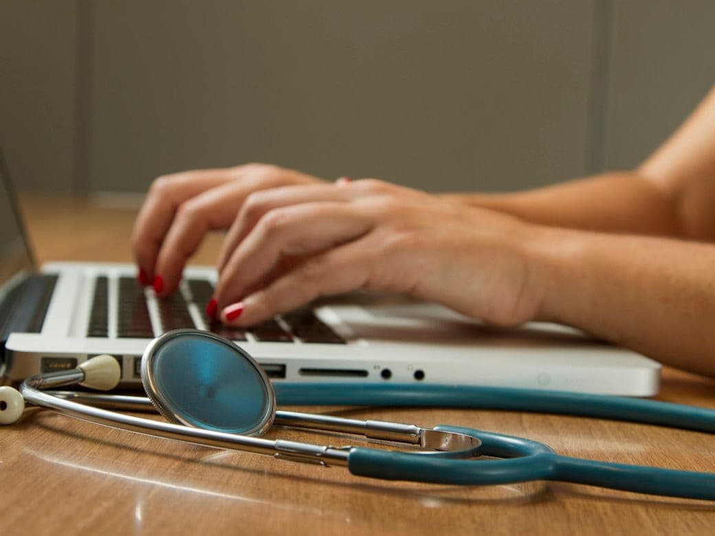 A clinician at a laptop, a stethoscope beside it